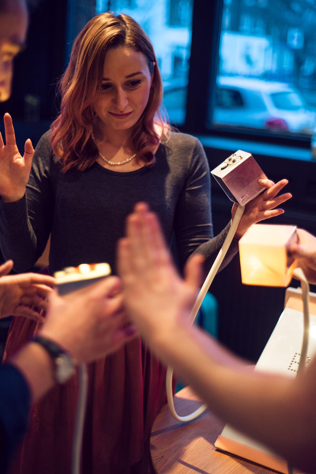 Three people holding little 8x8cm boxes reaching out to touch each other with their hands in a circle. 