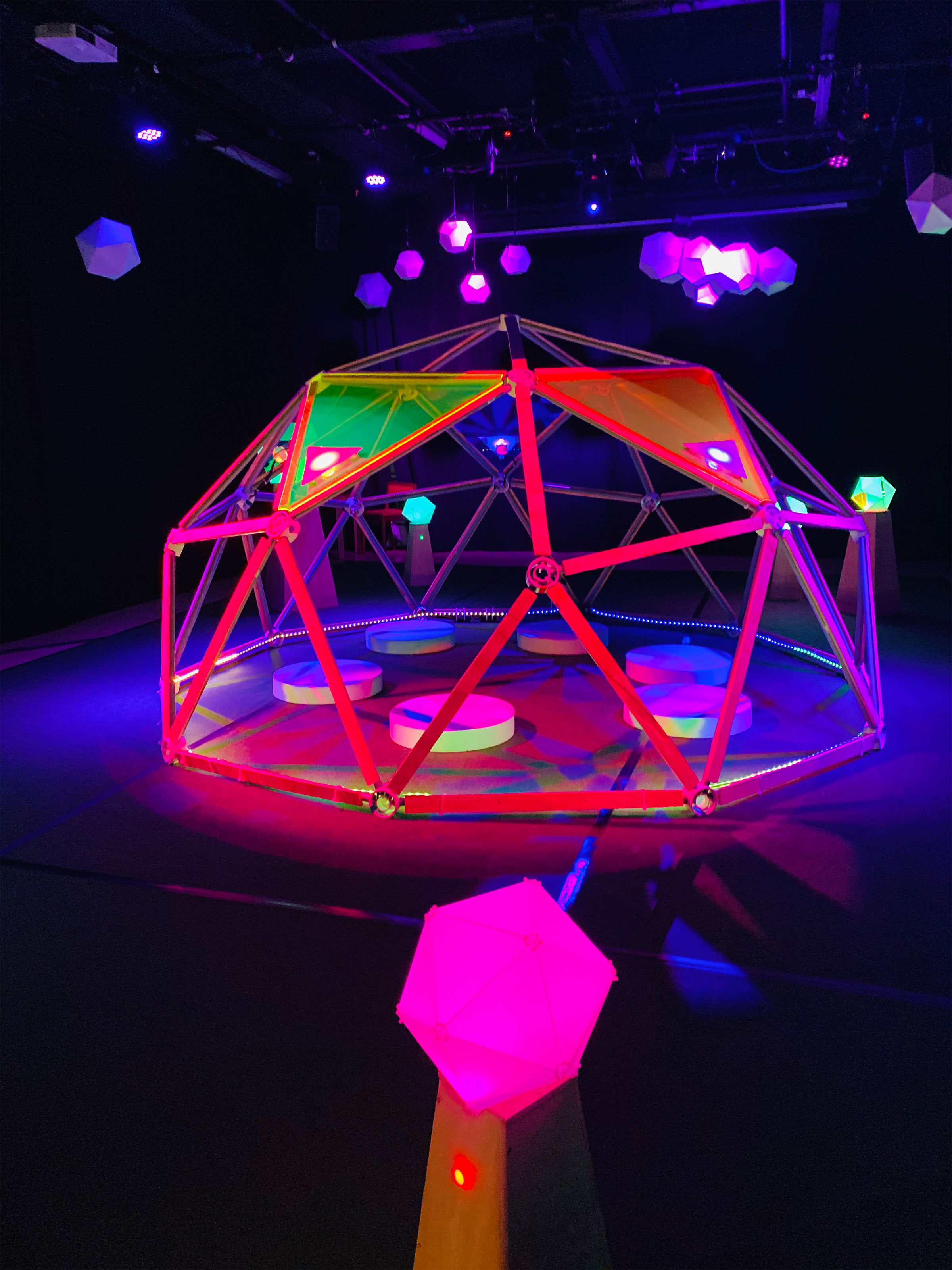 A geodesic dome in a black room lit by pink lights invites players inside.