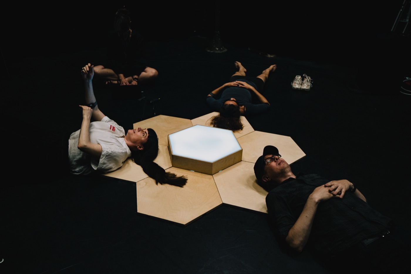 Four participants lying around the hexagonal tile grid, the central tile glowing white