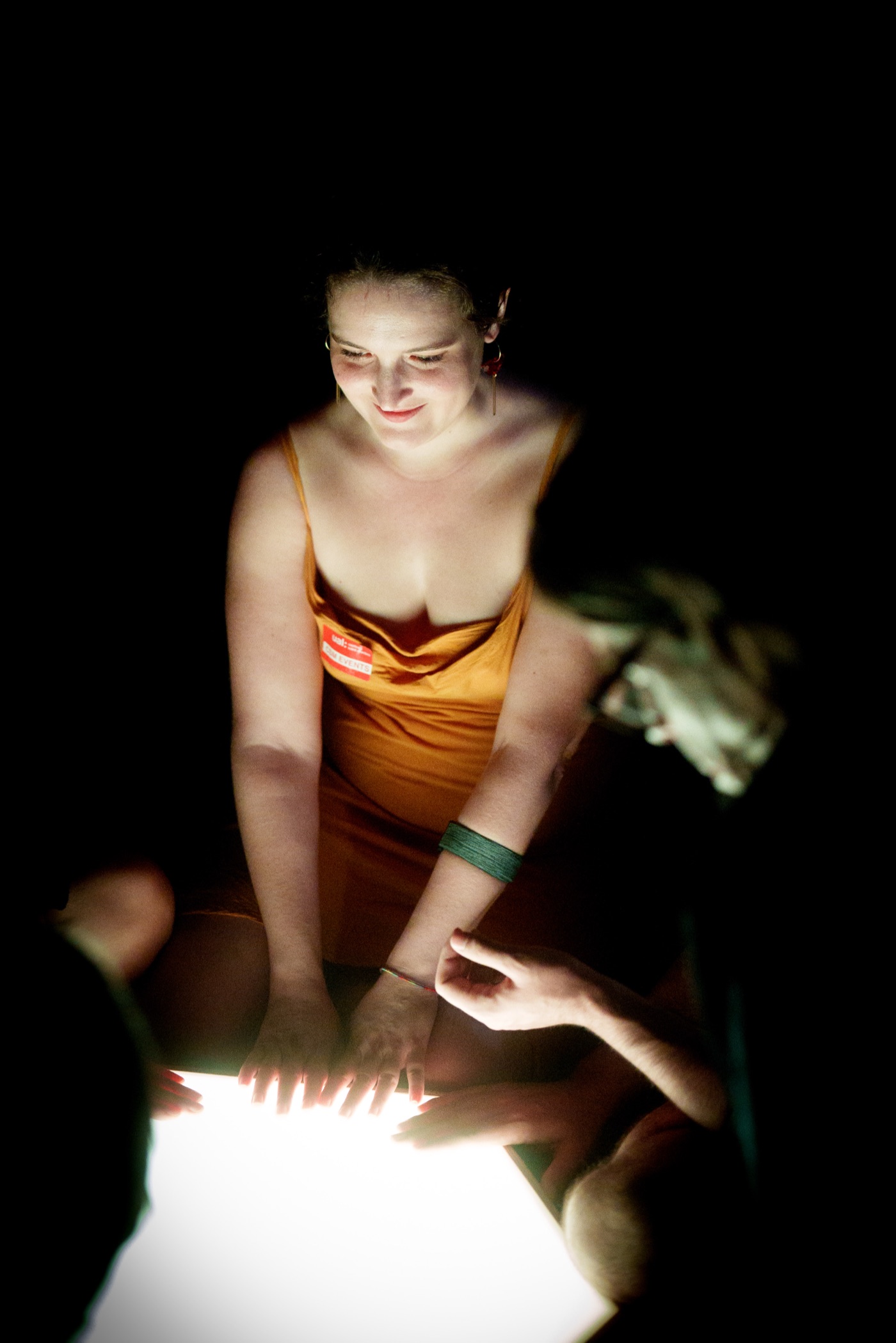 A participant lit by the glow of the central acrylic tile, hands resting on its surface