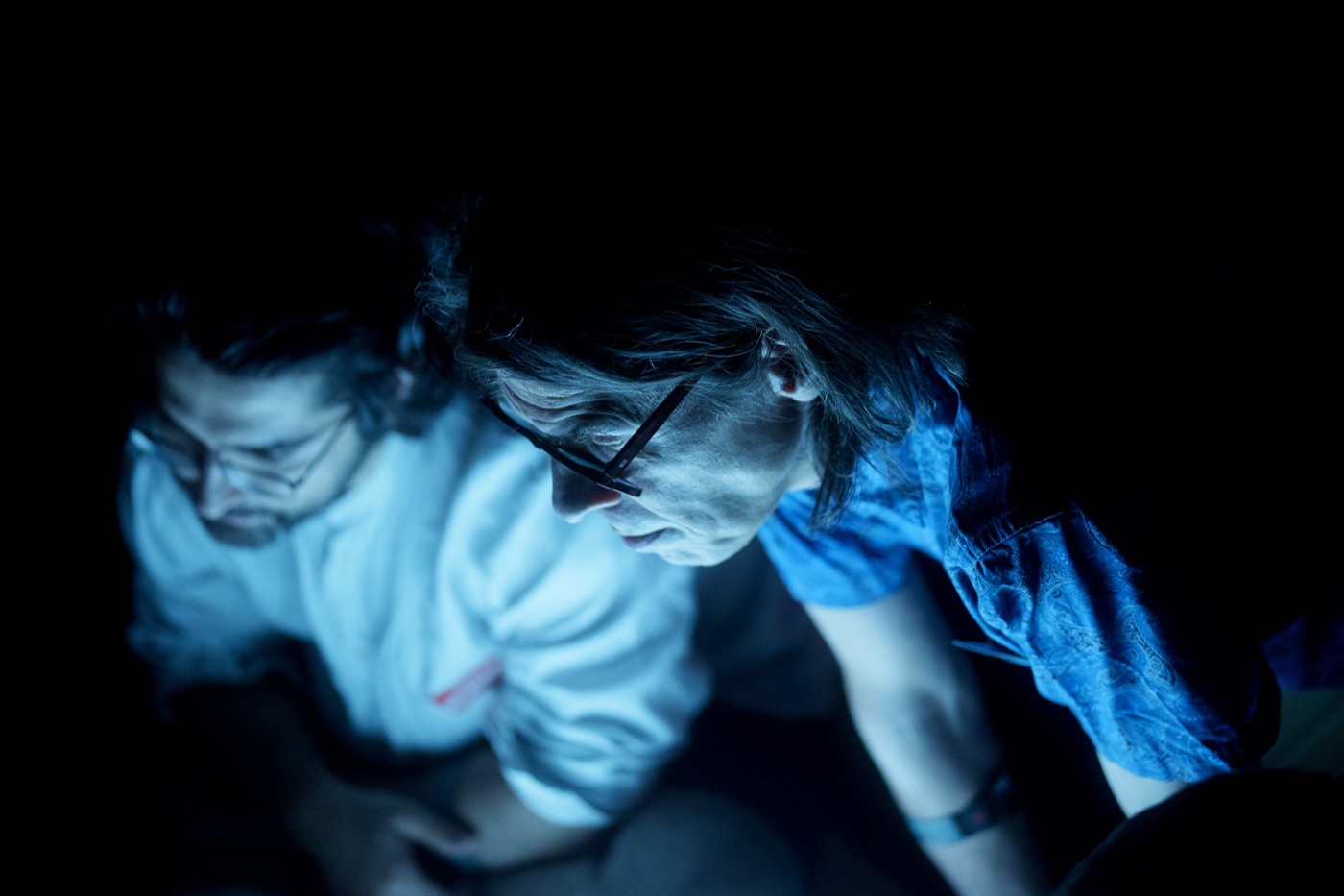 Two participants lit in cool blue light, close together and contemplative