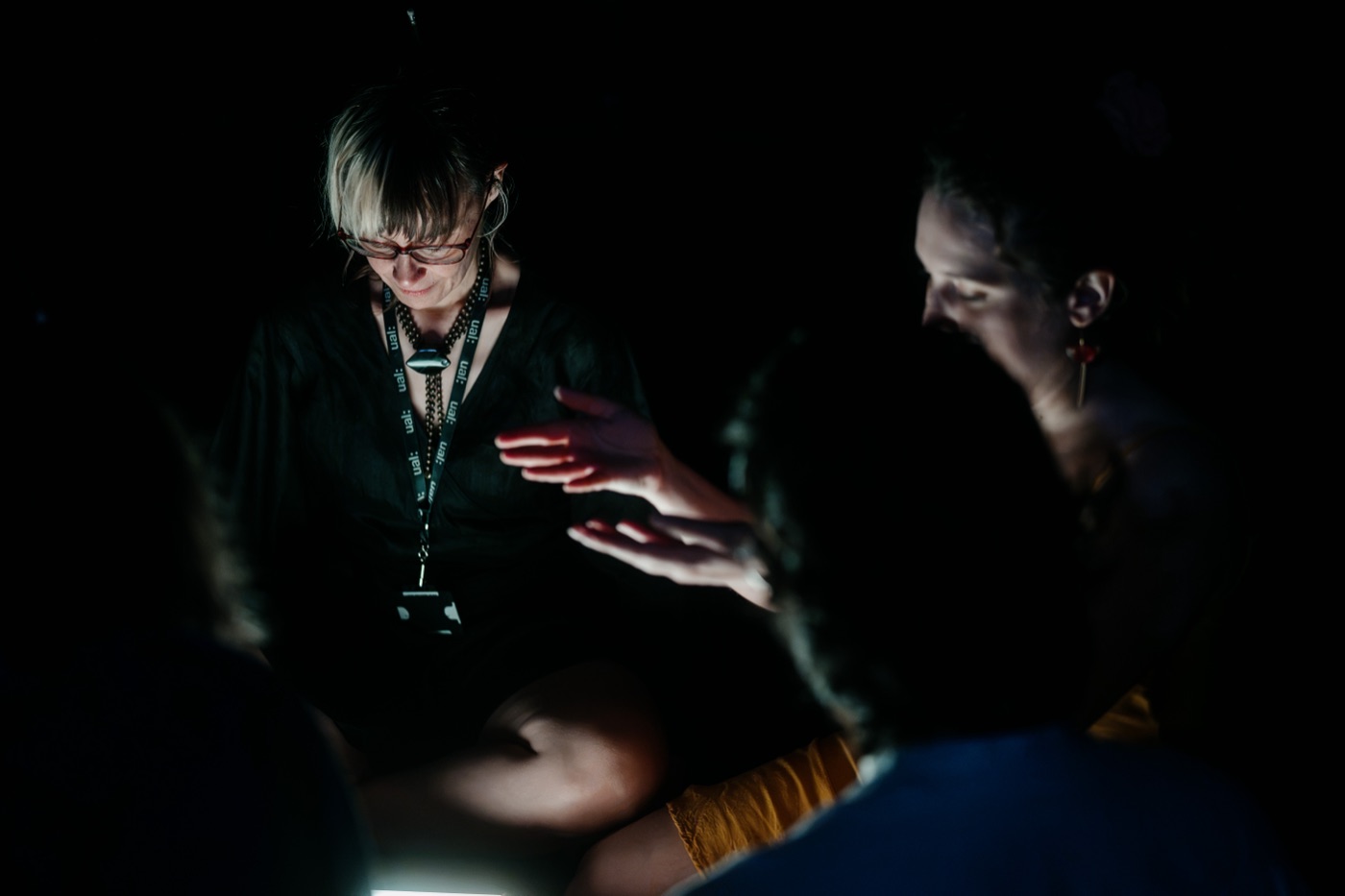 Hands gesturing over the glowing tile as the group gathers in the dark